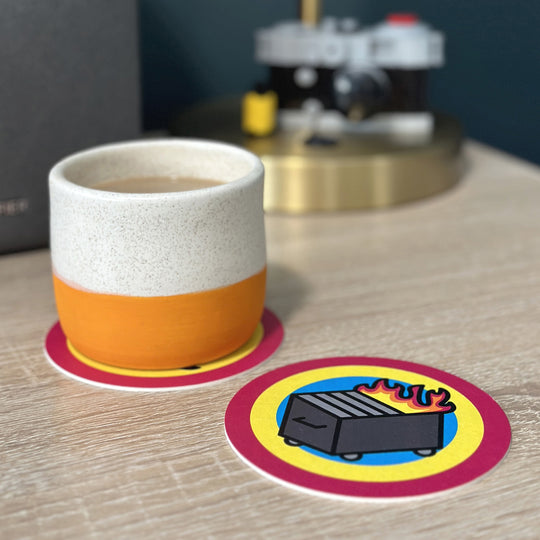Two dumpster fire coasters, one with a mug on it