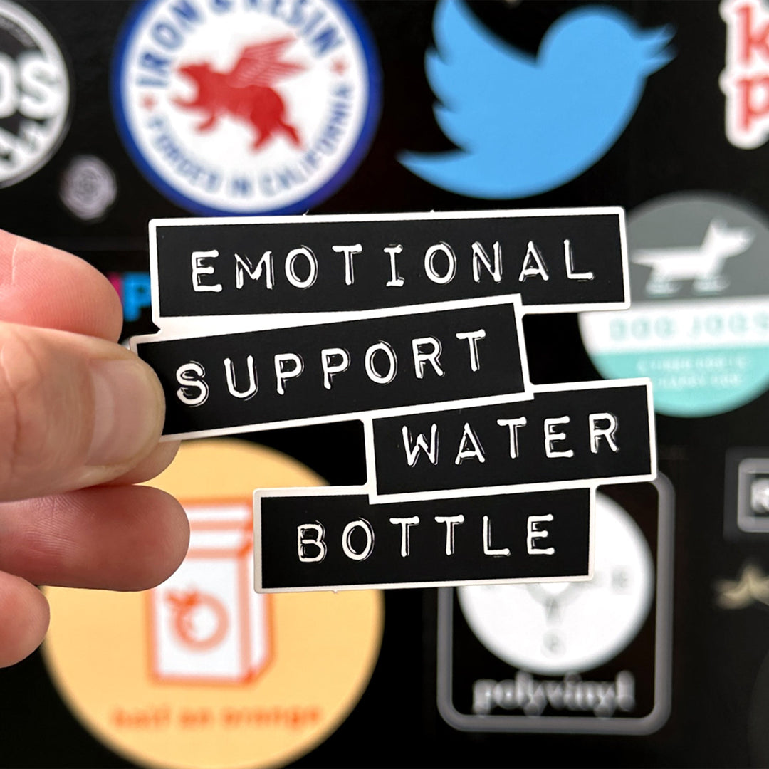 Emotional support water bottle sticker being held with a sticker door in the background